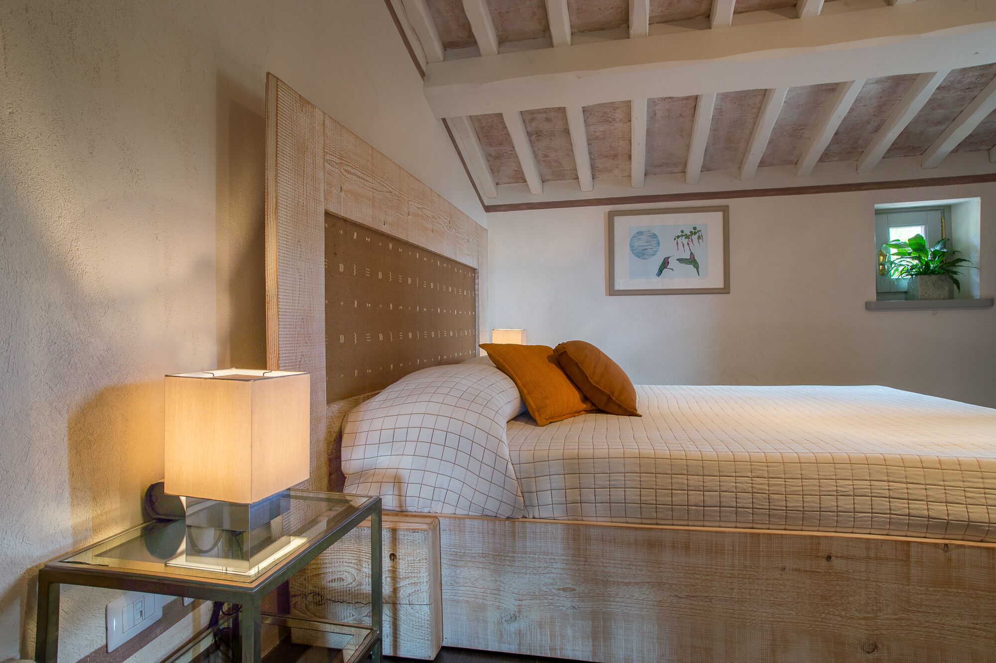 A bedroom with a wooden headboard, a bedside table with a lamp, a bed with a quilted cover, and a framed picture on the wall.