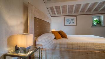 A bedroom with a wooden headboard, a bedside table with a lamp, a bed with a quilted cover, and a framed picture on the wall.