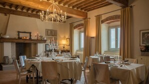A dining area with multiple round tables set for a meal, featuring a chandelier, a fireplace, and a view of the outdoors through large windows. - B&B La Dispensa (Lamporecchio)