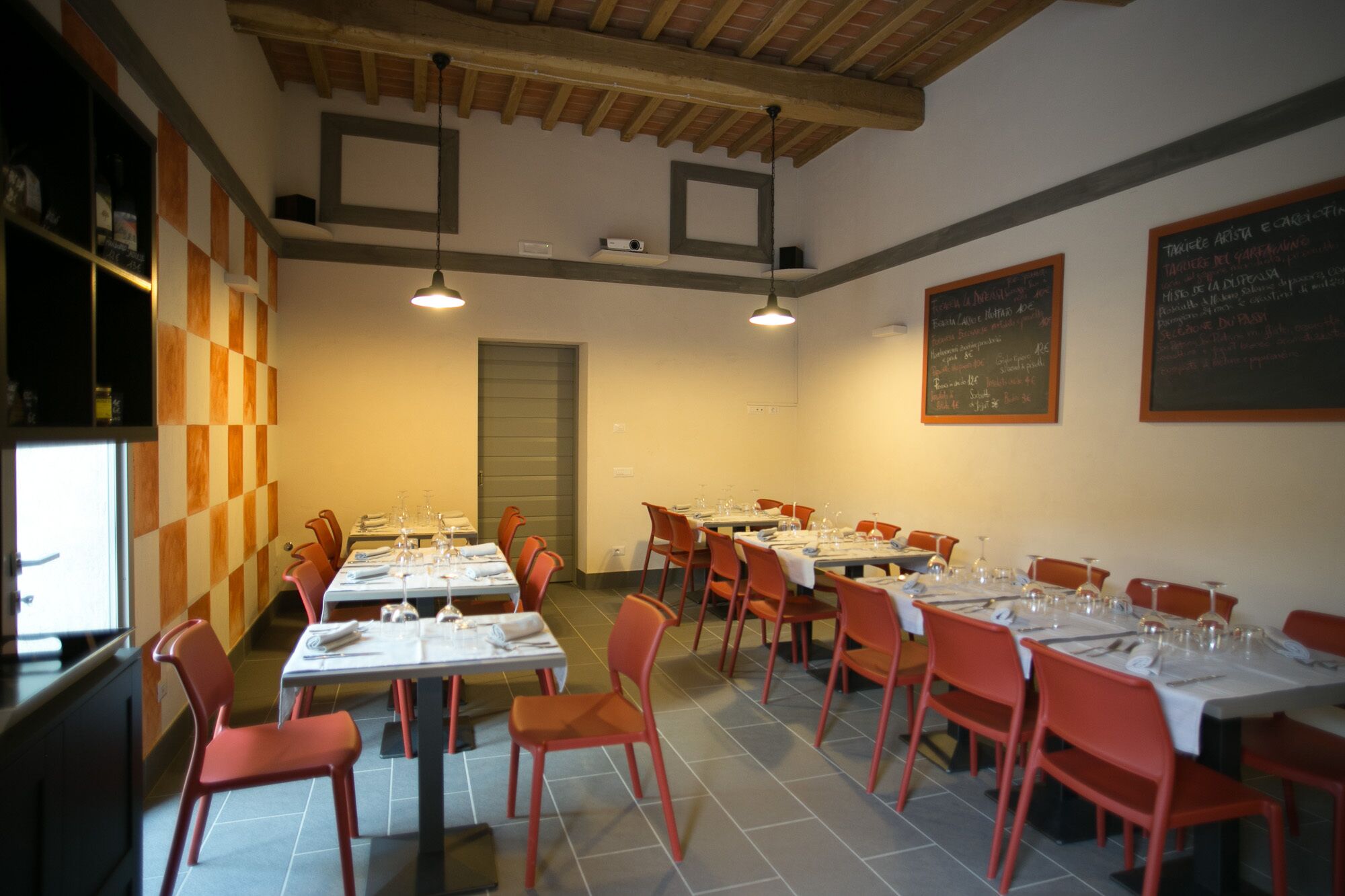 A restaurant with multiple tables set for dining, red chairs, and a high ceiling with exposed beams.