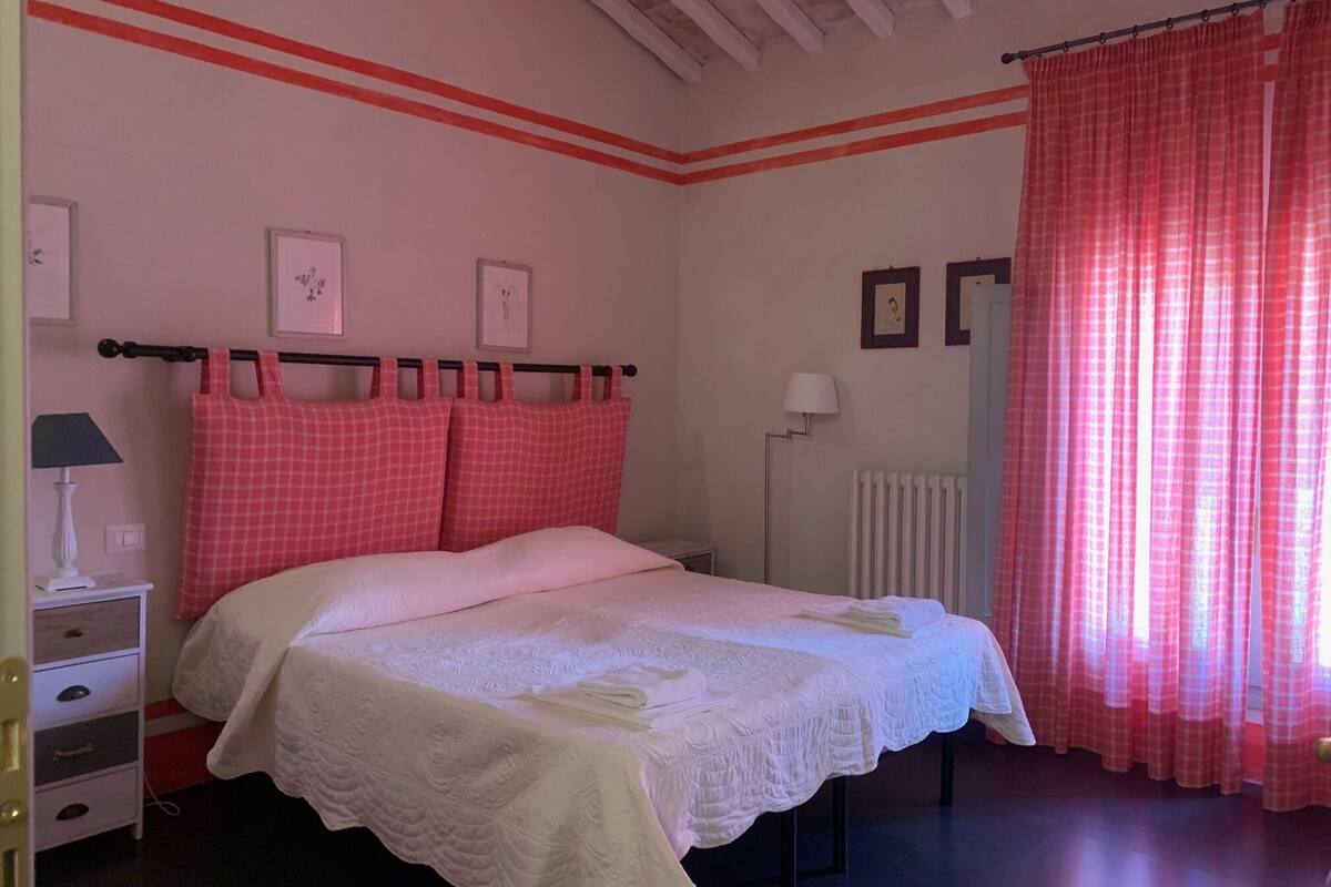 A bedroom with a bed, a nightstand, a lamp, a radiator, and curtains.