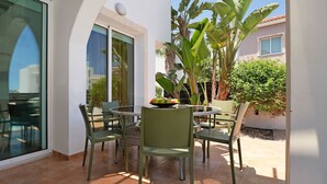 An outdoor patio with a round table and chairs, surrounded by plants and a view of a building. - MADISON - 3Bed Villa with private pool within walking distance to Pernera Resort Center (Paralimni)