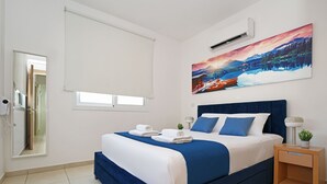 A bedroom with a large bed, a nightstand, a wall-mounted air conditioner, a window with a blind, and a painting above the bed. - MADISON - 3Bed Villa with private pool within walking distance to Pernera Resort Center (Paralimni)
