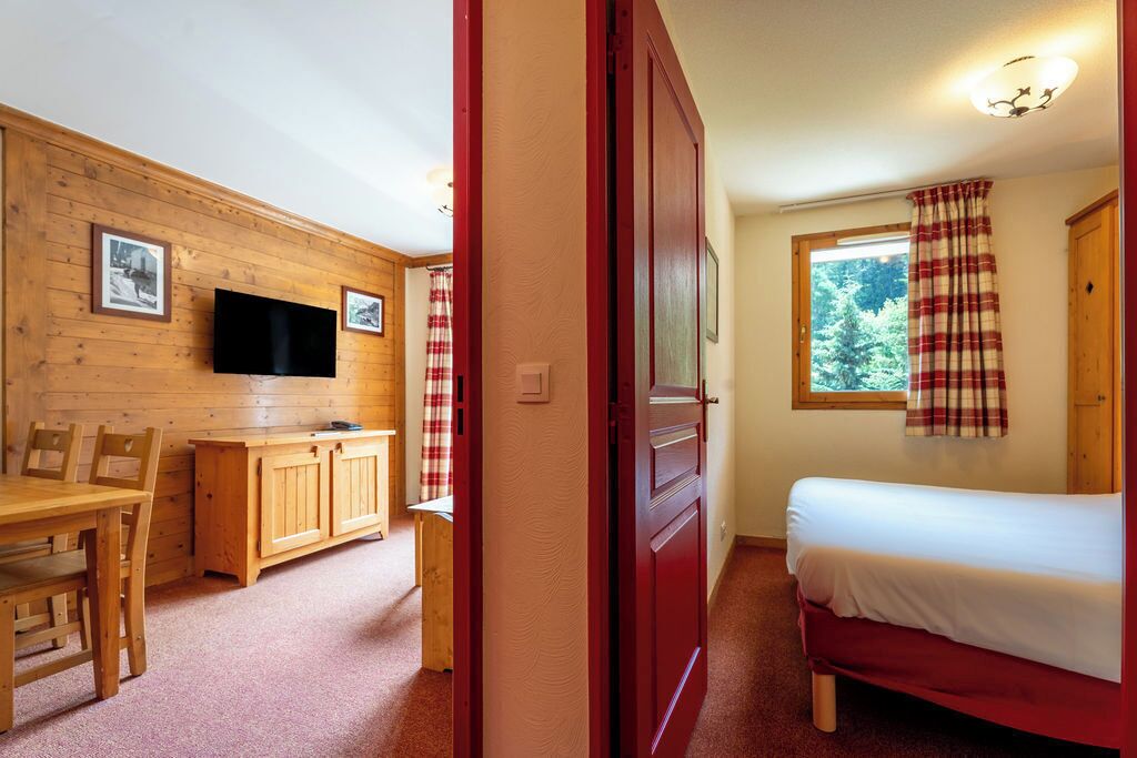A room with a wooden wall, a bed, a TV, a desk, and a window with curtains.