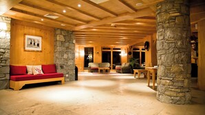 A spacious lobby with a wooden ceiling, stone pillars, a red sofa, and a stone fireplace. - travelski home premium - Résidence Les Alpages de Val Cenis 4* (Val-Cenis)