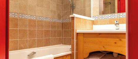 Un baño con bañera, tocador de madera y zona de ducha con azulejos.