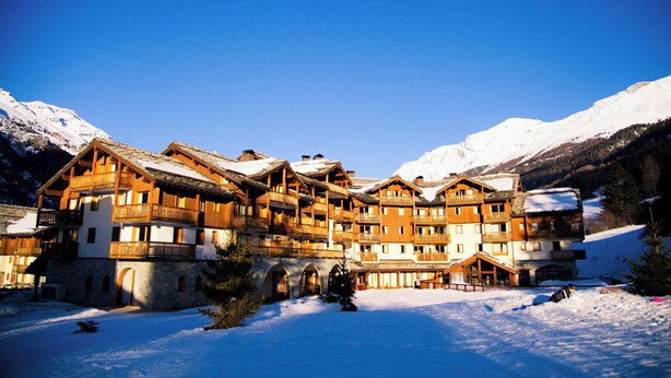 A large wooden hotel with multiple balconies and a snow-covered mountain backdrop. - travelski home premium - Résidence Les Alpages de Val Cenis 4* (Val-Cenis)