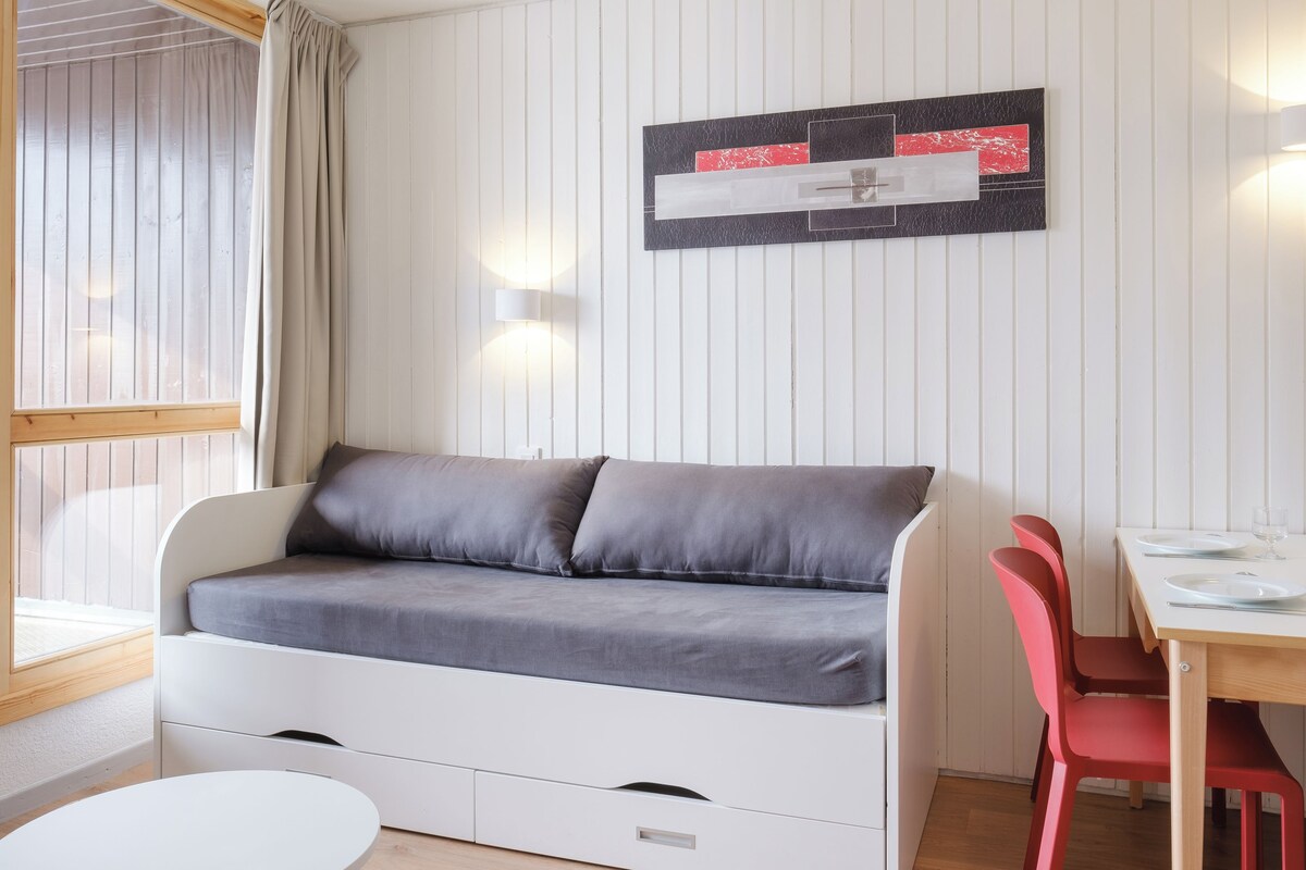 Une pièce avec un canapé blanc, une table à manger entourée de chaises rouges et un luminaire fixé au mur.