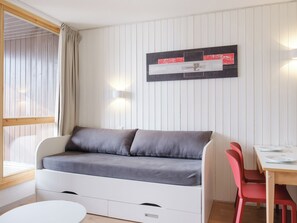 Une pièce avec un canapé blanc, une table à manger entourée de chaises rouges et un luminaire fixé au mur.