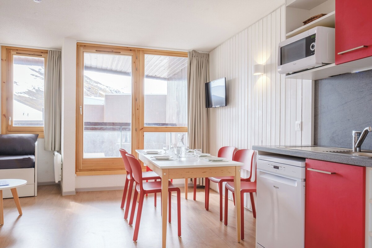 Une cuisine moderne équipée d’un four à micro-ondes, d’un évier et d’un lave-vaisselle. On y trouve également un coin repas avec une table et des chaises, ainsi qu’un téléviseur fixé au mur.