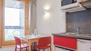 Uma cozinha compacta com micro-ondas, pia e lava-louças. Há uma mesa de jantar com duas cadeiras e uma janela com cortinas.