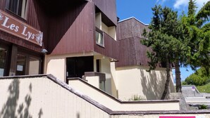 Ένα κτίριο με μια πινακίδα που γράφει «Les Lys» και μια άλλη πινακίδα που υποδεικνύει την πρόσβαση στα τελεφερίκ του σκι και σε ένα άλλο κτίριο.