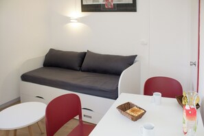 Ein gemütlicher Raum mit Schlafsofa, Esstisch, zwei Stühlen und einem kleinen Tisch mit Korb und Glas.