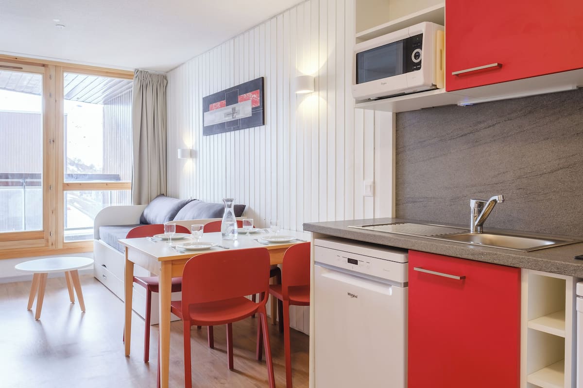 Une cuisine moderne équipée d’un four à micro-ondes, d’un évier et d’un lave-vaisselle. Un coin repas avec une table et des chaises est également à disposition.