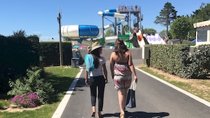 A pathway with a water park in the background, including a water slide and a large water tank. - Camping Club Sunissim Le Trianon (Les Sables-d'Olonne)