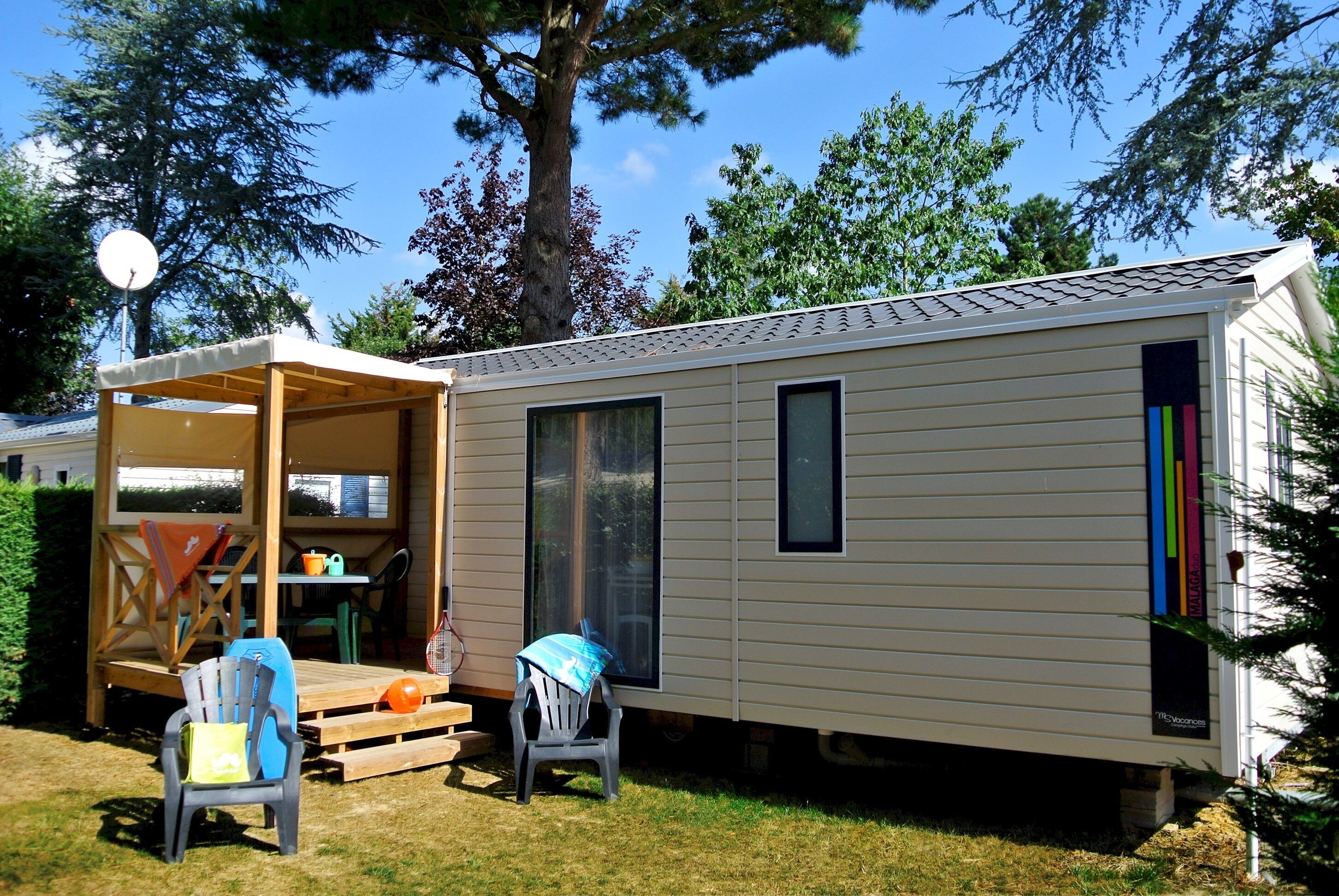 A mobile home with a covered patio, two chairs, a table, and a satellite dish.