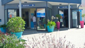A reception area with glass doors, potted plants, and signage for reception and location. - Camping Club Sunissim Le Trianon (Les Sables-d'Olonne)