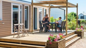A wooden deck with a pergola, outdoor seating, and flower planters. - Camping Sunissim Le Domaine Les Mûriers (Vendres)