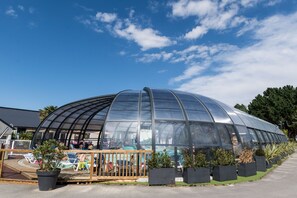 A large greenhouse structure with a curved glass roof, surrounded by potted plants and a wooden deck area. - Camping Sunissim Emeraude (Saint-Briac-sur-Mer)
