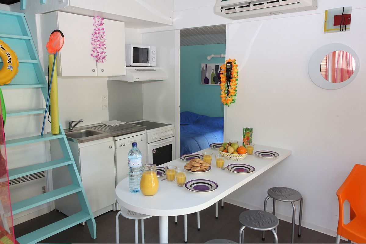 A compact kitchen with a microwave, sink, and a small dining table set with plates, glasses, and a fruit bowl.