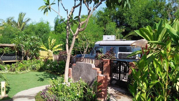 A garden with a concrete pathway, a brick wall, and a blue vehicle parked near a gate.