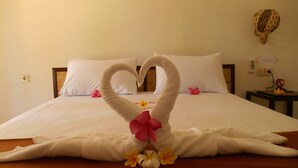 A bed with a heart-shaped towel arrangement and flowers.