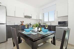 A modern kitchen with white cabinets, a dining table with blue placemats, and a built-in oven.