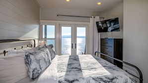 Une chambre avec un grand lit, un téléviseur fixé au mur et une vue sur la mer par les fenêtres.