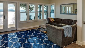 Un salon doté d’une grande fenêtre donnant sur un plan d’eau, d’un canapé marron et d’un tapis bleu à motifs.
