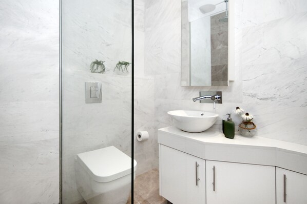 Une salle de bain moderne avec une douche à parois de verre, des toilettes blanches, un lavabo avec un plan de toilette en marbre et un miroir au-dessus du lavabo.