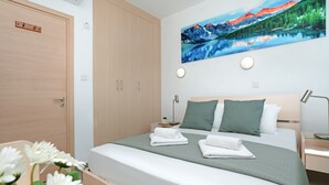 A modern hotel room with a large bed, a nightstand, a desk, and a painting of a mountain landscape.