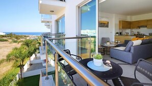 A modern apartment with a balcony overlooking a beach, a kitchen with wooden cabinets, and a living area with a sofa and coffee table.