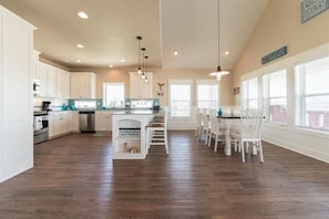 A spacious kitchen with white cabinets, a central island, and a dining area with white chairs. - Bienvenu To The Beach - 3 Bedroom - Sleeps 10 - Beautiful beach house!! (Crystal Beach)