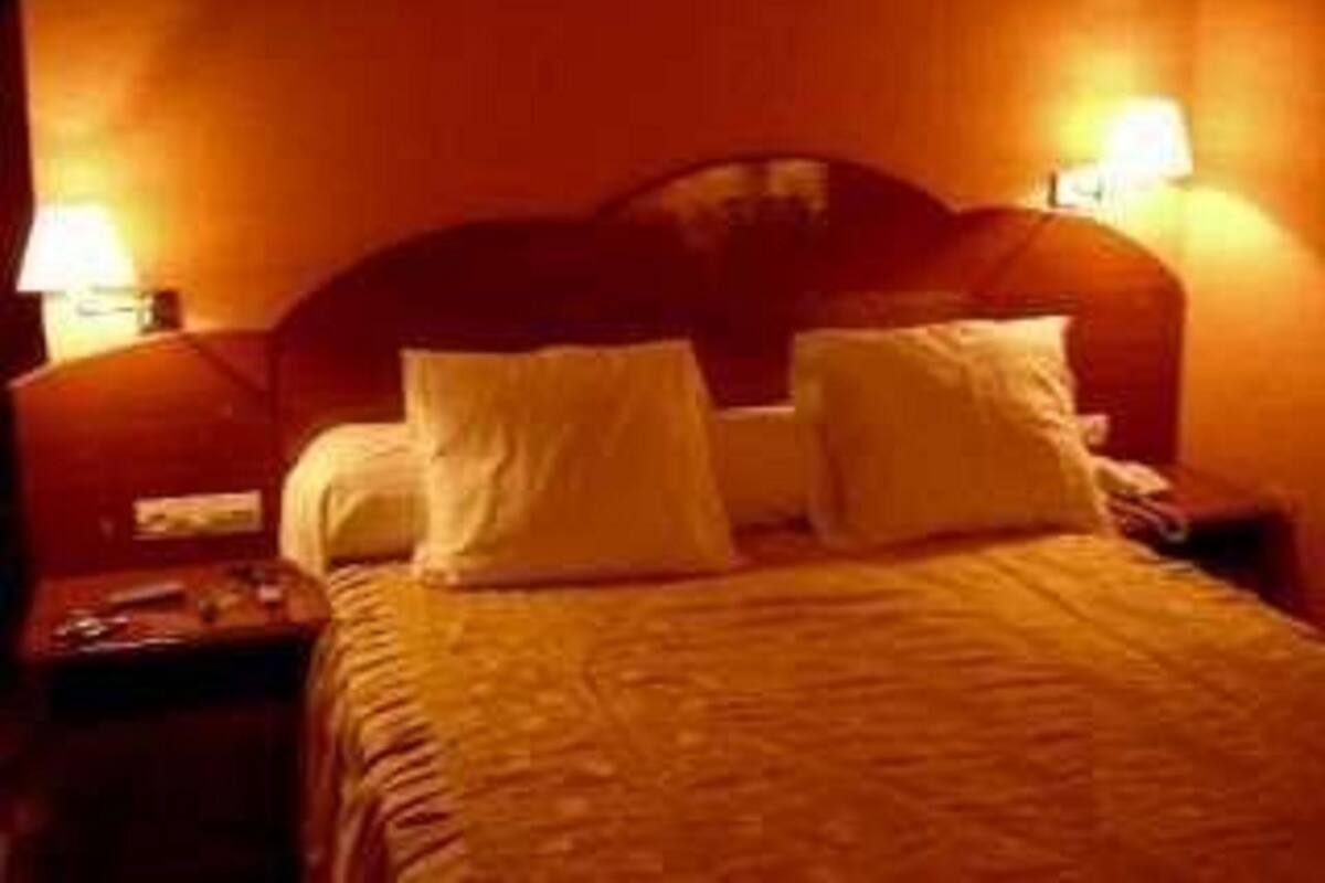 A hotel room with a wooden headboard, two bedside tables, and a bed with a patterned bedspread.