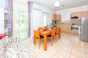 A modern kitchen with wooden cabinets, a dining table with chairs, and a built-in oven. - Villa Natalie - Walking to Fig Tree Bay (Paralimni)