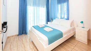 Una cama bien hecha con colcha azul y almohadas blancas, una mesita de noche con lámpara y un teléfono instalado en la pared.