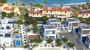 Un quartier résidentiel en bord de mer, avec des immeubles d’appartements modernes, une piscine et une plage en arrière-plan.