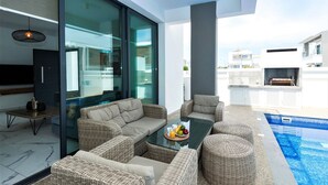 Un espace de vie extérieur moderne, avec des meubles en osier, une table en verre ornée de fruits et une piscine.