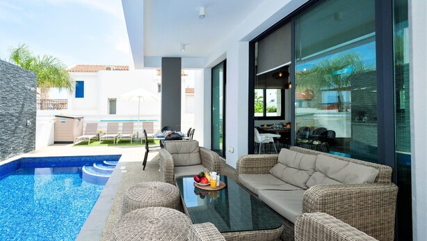 Un espace de vie extérieur moderne, doté d'une piscine, de meubles en osier et d'une table en verre sur laquelle sont disposés des fruits.