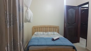 Ein Schlafzimmer mit einem hölzernen Bett, einer zusammengerollten Decke und einem weißen Vorhang.