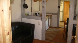 A compact living space with a black leather sofa, a kitchenette with basic appliances, and a wooden dining table. - Vacation under thatch (Postfeld)