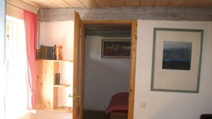 A room with a wooden door leading to another room, a small table, and a framed picture on the wall. - Vacation under thatch (Postfeld)