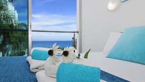 A hotel room with a large window, a bed with white and blue bedding, and a view of the ocean. - NIOVI Sea View Aprt - Coralli Beachfront Resort (Paralimni)
