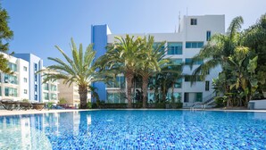 Ein Swimmingpool mit klarem, blauem Wasser, umgeben von Palmen und modernen Gebäuden.
