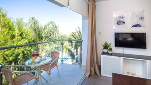 Ein Balkon mit Korbstühlen, einem Tisch mit Obst und Getränken, einem Fernseher und Bildern an der Wand.