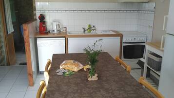 Keittiössä on ruokapöytä, tuoleja, kahvinkeitin, vedenkeitin, mikroaaltouuni, pesuallas ja liesi.