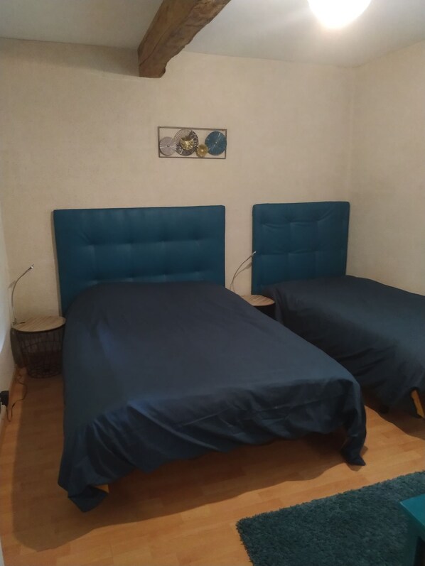 A room with two beds, a small round table, a wall-mounted decoration, and a wooden floor.