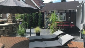 En uteplats med en eldstad i sten, loungestolar och parasoller.