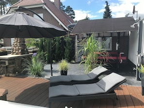 Een terras met een stenen open haard, lounge stoelen en parasols.