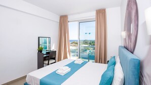 A hotel room with a large bed, a desk, a chair, and a view of the ocean. - Sharon Sea View - Coralli BeachFront Resort (Paralimni)